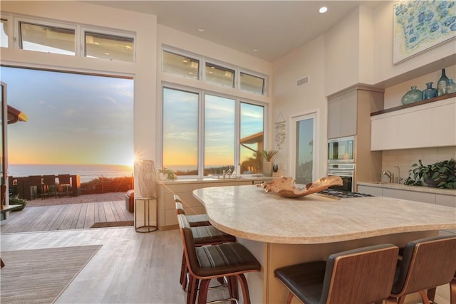 kitchen featuring a breakfast bar area, appliances with stainless steel finishes, white cabinetry, a high ceiling, and light hardwood / wood-style floors