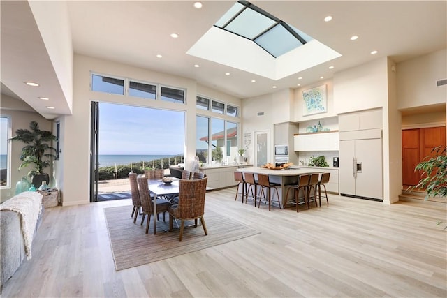 dining room with a high ceiling, a water view, and light hardwood / wood-style floors