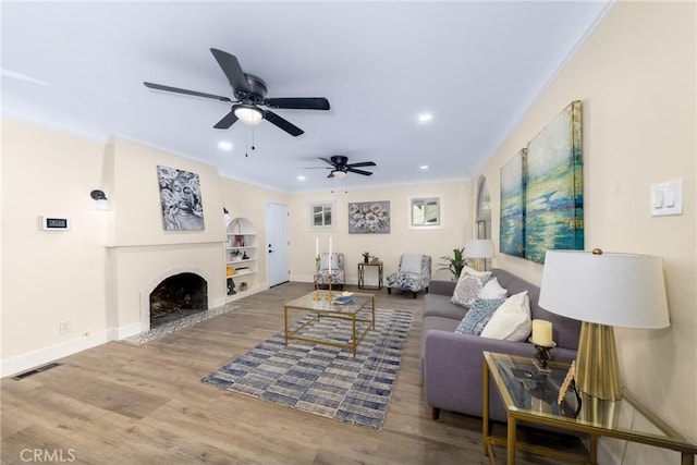 living room with ceiling fan, ornamental molding, built in features, and hardwood / wood-style flooring