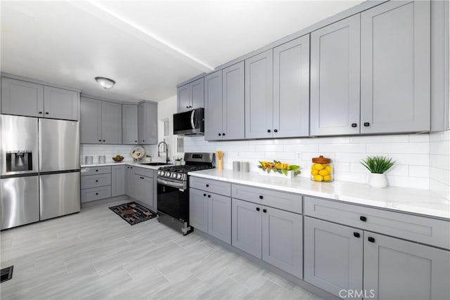 kitchen with sink, backsplash, gray cabinetry, and appliances with stainless steel finishes