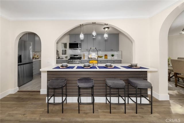 bar with decorative light fixtures, hardwood / wood-style floors, decorative backsplash, gray cabinetry, and appliances with stainless steel finishes