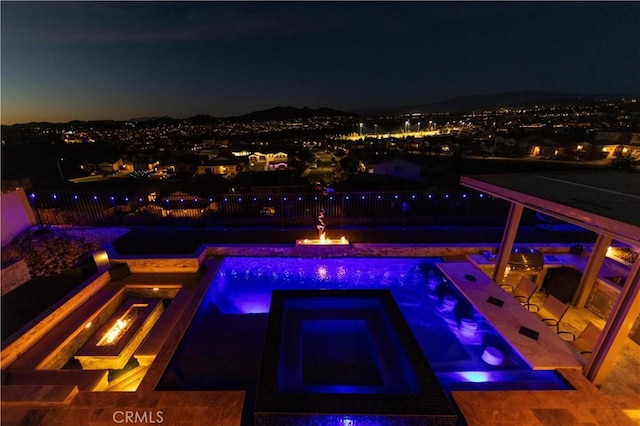 pool at night featuring an in ground hot tub and a fire pit