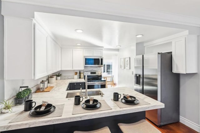 kitchen featuring white cabinets, stainless steel appliances, sink, a kitchen breakfast bar, and kitchen peninsula