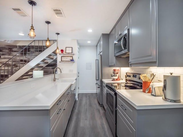 kitchen with stainless steel appliances, sink, hanging light fixtures, gray cabinets, and dark hardwood / wood-style flooring