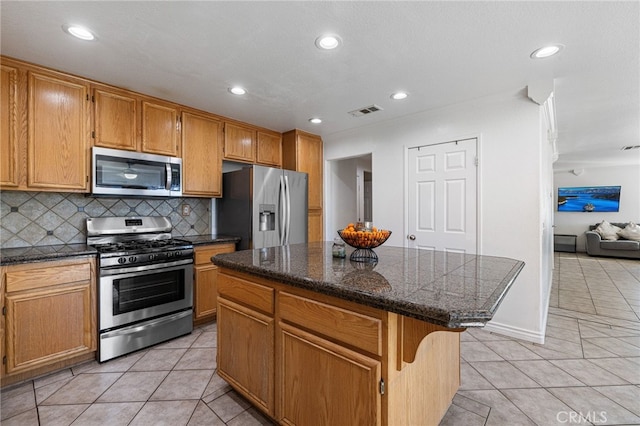 kitchen featuring light tile patterned floors, appliances with stainless steel finishes, backsplash, and a center island