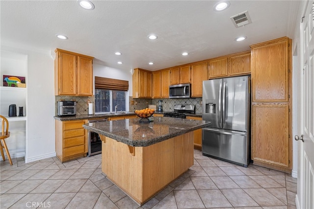 kitchen featuring appliances with stainless steel finishes, a kitchen island, dark stone countertops, decorative backsplash, and a breakfast bar