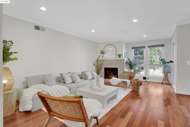 living room with a high end fireplace, ornamental molding, and light hardwood / wood-style flooring