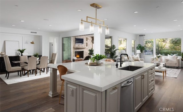 kitchen with a large fireplace, decorative light fixtures, a center island with sink, a kitchen bar, and sink