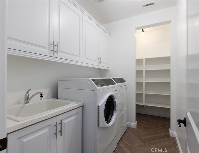 laundry area with dark parquet flooring, cabinets, washing machine and clothes dryer, and sink