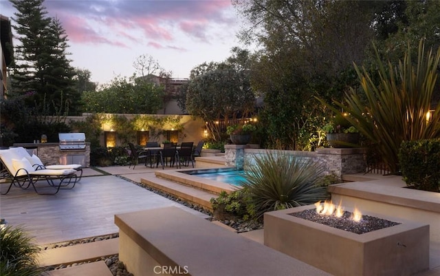 pool at dusk featuring grilling area, an outdoor fire pit, a patio, and area for grilling