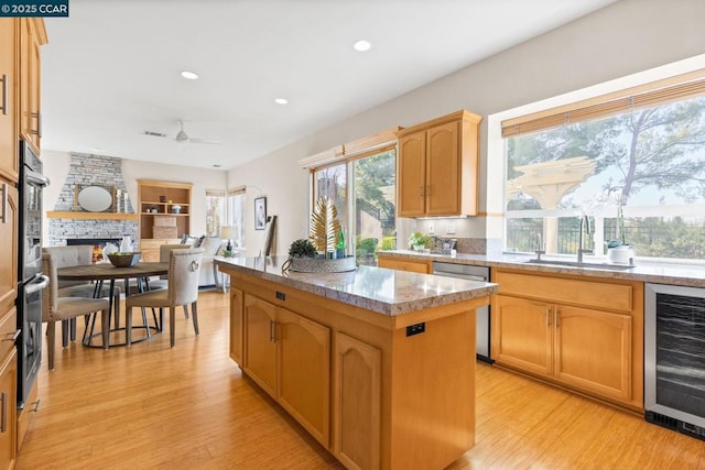 kitchen featuring beverage cooler, stainless steel appliances, a kitchen island, a fireplace, and sink