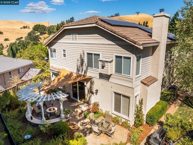 back of house with a fire pit, solar panels, a mountain view, and a patio area