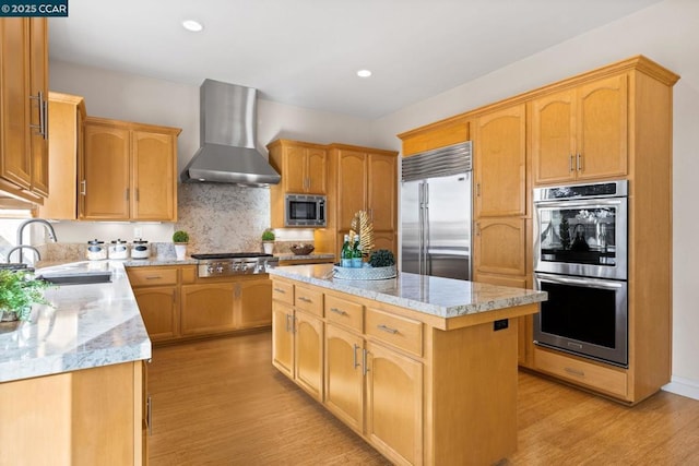 kitchen featuring a center island, built in appliances, light stone counters, sink, and wall chimney range hood