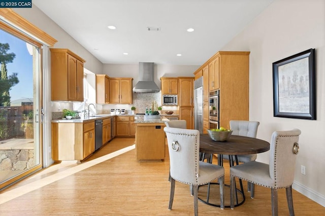 kitchen with light wood-type flooring, a center island, built in appliances, wall chimney range hood, and tasteful backsplash