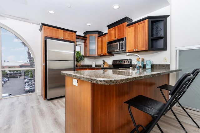 kitchen featuring light hardwood / wood-style flooring, kitchen peninsula, dark stone counters, a breakfast bar, and appliances with stainless steel finishes