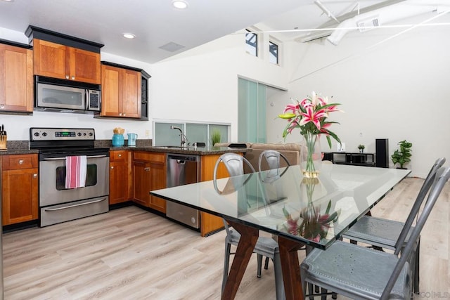 kitchen featuring dark stone countertops, appliances with stainless steel finishes, light wood-type flooring, kitchen peninsula, and sink