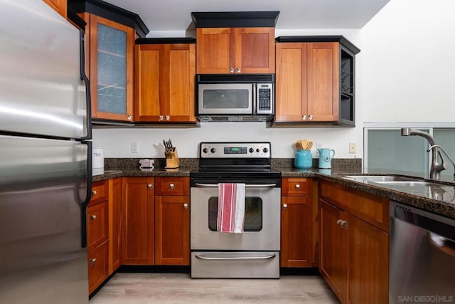 kitchen with sink, dark stone countertops, light wood-type flooring, and appliances with stainless steel finishes