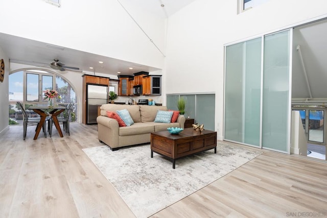 living room with a towering ceiling, ceiling fan, and light hardwood / wood-style floors