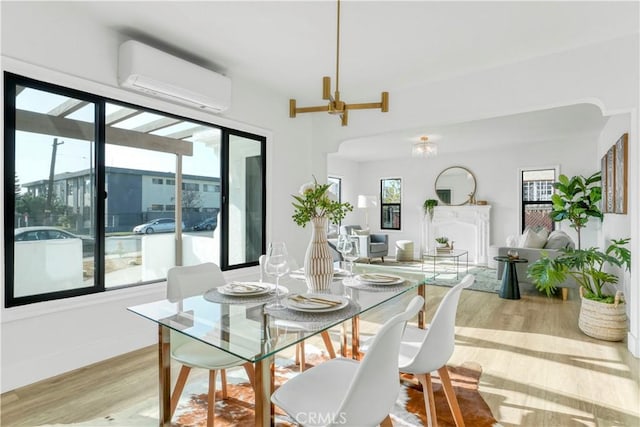 dining room featuring a chandelier, a wall mounted air conditioner, a wealth of natural light, and light hardwood / wood-style flooring