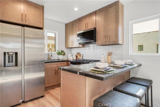 kitchen with sink, a kitchen bar, light wood-type flooring, backsplash, and appliances with stainless steel finishes