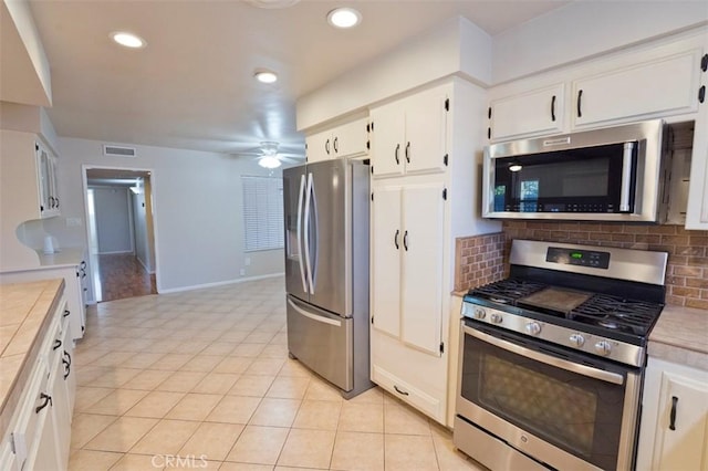 kitchen featuring backsplash, tile countertops, light tile patterned floors, appliances with stainless steel finishes, and white cabinets