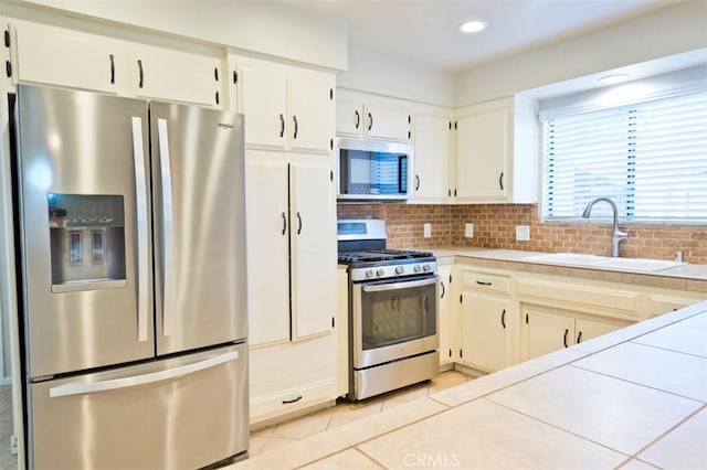 kitchen with tasteful backsplash, sink, white cabinetry, stainless steel appliances, and tile counters