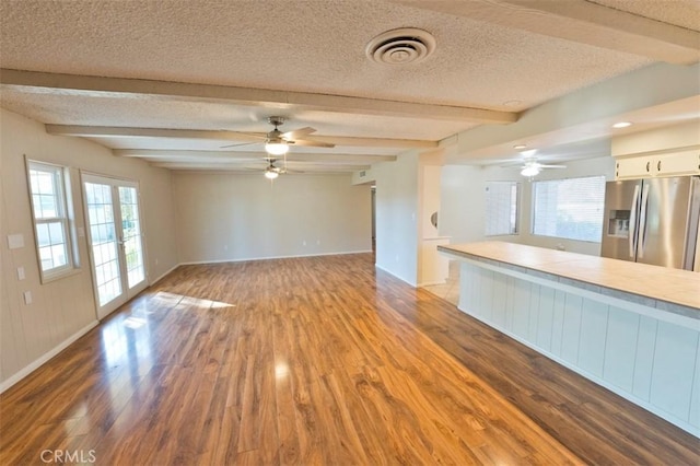 unfurnished living room featuring light hardwood / wood-style floors, ceiling fan, french doors, a textured ceiling, and beamed ceiling