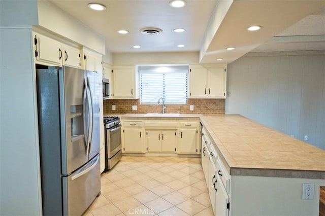 kitchen with tasteful backsplash, kitchen peninsula, sink, stainless steel appliances, and light tile patterned floors