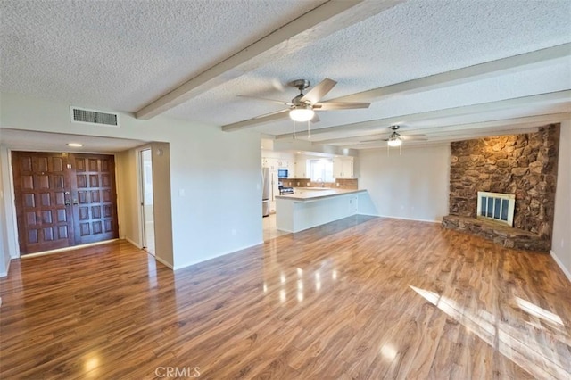 unfurnished living room featuring a textured ceiling, beamed ceiling, a fireplace, ceiling fan, and hardwood / wood-style flooring