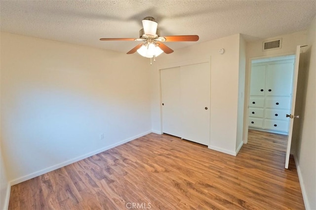 unfurnished bedroom featuring ceiling fan, a textured ceiling, wood-type flooring, and a closet