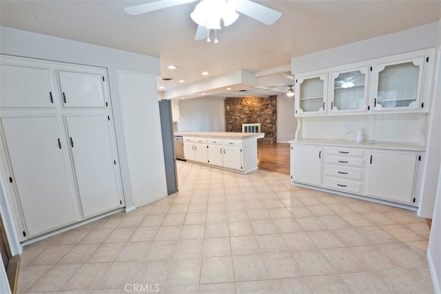 kitchen featuring ceiling fan, kitchen peninsula, light tile patterned floors, a stone fireplace, and white cabinets