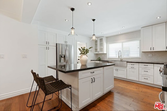 kitchen featuring a breakfast bar area, wood-type flooring, a center island, stainless steel fridge, and white cabinetry