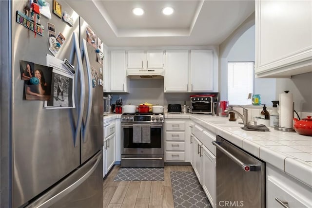 kitchen with a raised ceiling, sink, white cabinetry, appliances with stainless steel finishes, and tile counters