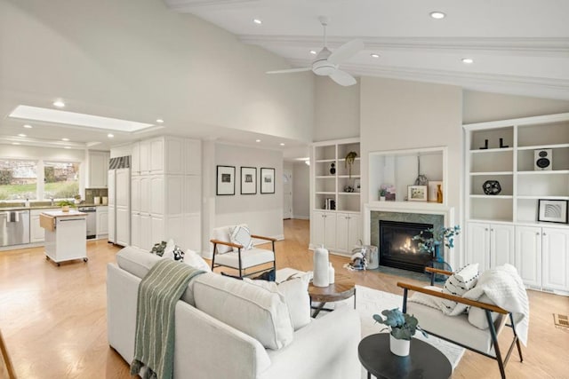 living room with ceiling fan, light hardwood / wood-style flooring, beam ceiling, and a premium fireplace