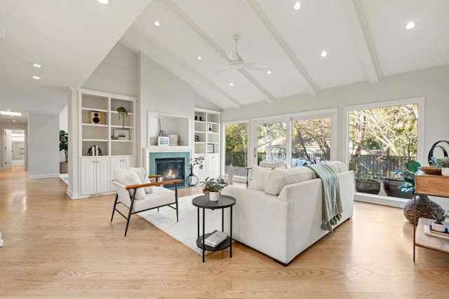 living room with ceiling fan, built in shelves, beamed ceiling, and light hardwood / wood-style floors