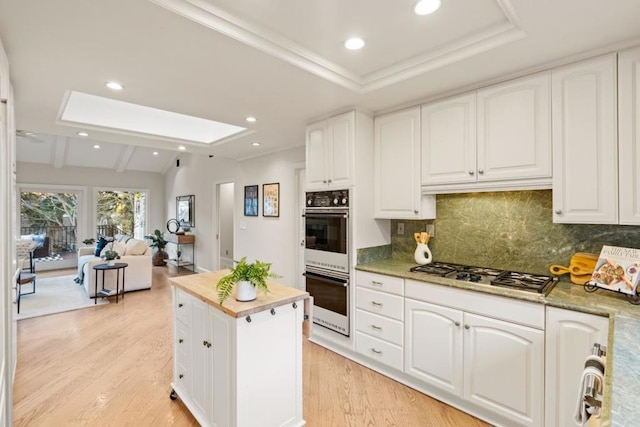 kitchen featuring vaulted ceiling with skylight, white cabinets, stainless steel gas stovetop, and double oven