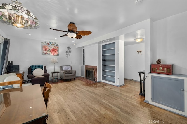 living room with a brick fireplace, ceiling fan, and light hardwood / wood-style floors