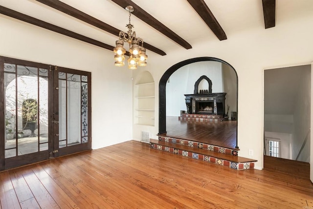 unfurnished living room with beam ceiling, a chandelier, hardwood / wood-style floors, and built in shelves