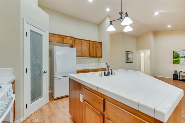 kitchen featuring white appliances, a center island with sink, light hardwood / wood-style floors, pendant lighting, and tile countertops