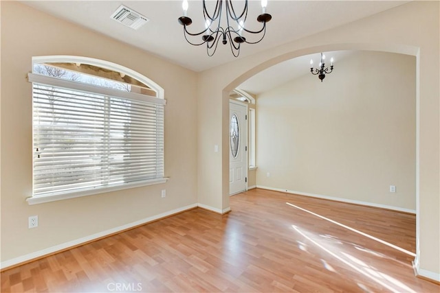 empty room featuring lofted ceiling, a chandelier, and hardwood / wood-style floors