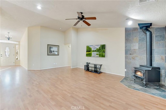 unfurnished living room featuring hardwood / wood-style flooring, a textured ceiling, a wood stove, lofted ceiling, and ceiling fan