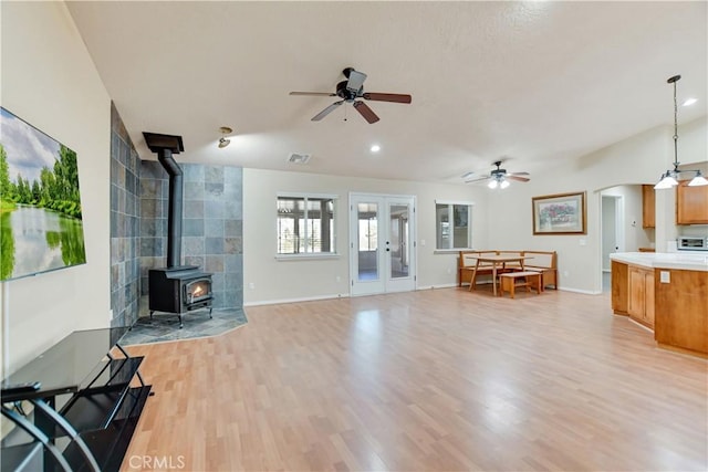 living room featuring french doors, ceiling fan, a wood stove, and light hardwood / wood-style flooring