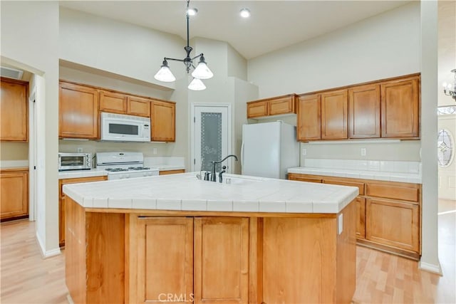 kitchen with white appliances, a kitchen island with sink, tile countertops, and sink