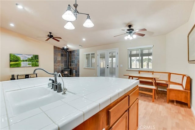 kitchen with sink, a wood stove, light hardwood / wood-style flooring, tile counters, and hanging light fixtures