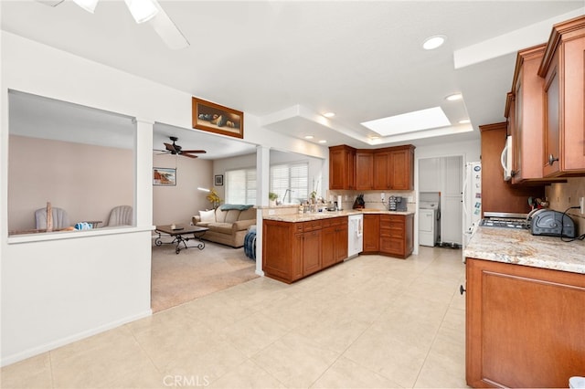 kitchen with ceiling fan, light colored carpet, white appliances, a tray ceiling, and light stone countertops