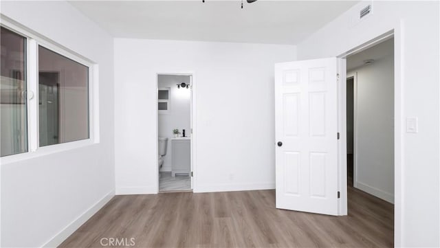 unfurnished bedroom featuring ensuite bathroom and light wood-type flooring