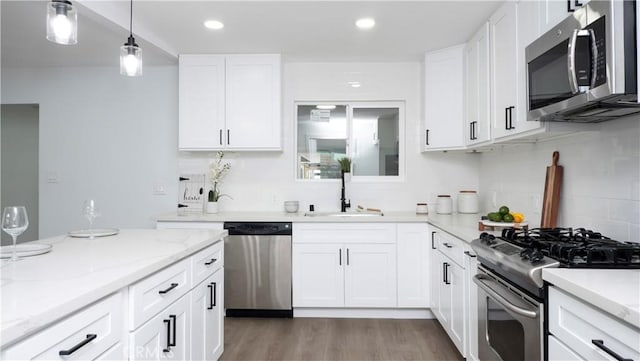 kitchen featuring light stone countertops, white cabinets, appliances with stainless steel finishes, sink, and hanging light fixtures