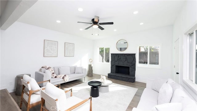 living room featuring ceiling fan, a stone fireplace, and hardwood / wood-style floors