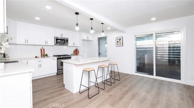 kitchen featuring light hardwood / wood-style floors, appliances with stainless steel finishes, decorative light fixtures, white cabinets, and a center island