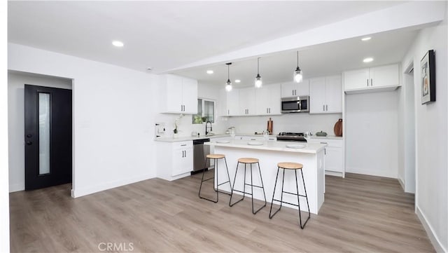 kitchen with white cabinetry, appliances with stainless steel finishes, decorative light fixtures, a kitchen island, and light hardwood / wood-style flooring